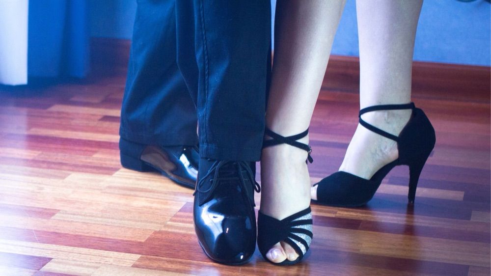 A couple's dance shoes side by side on a polished wooden floor mid-lesson